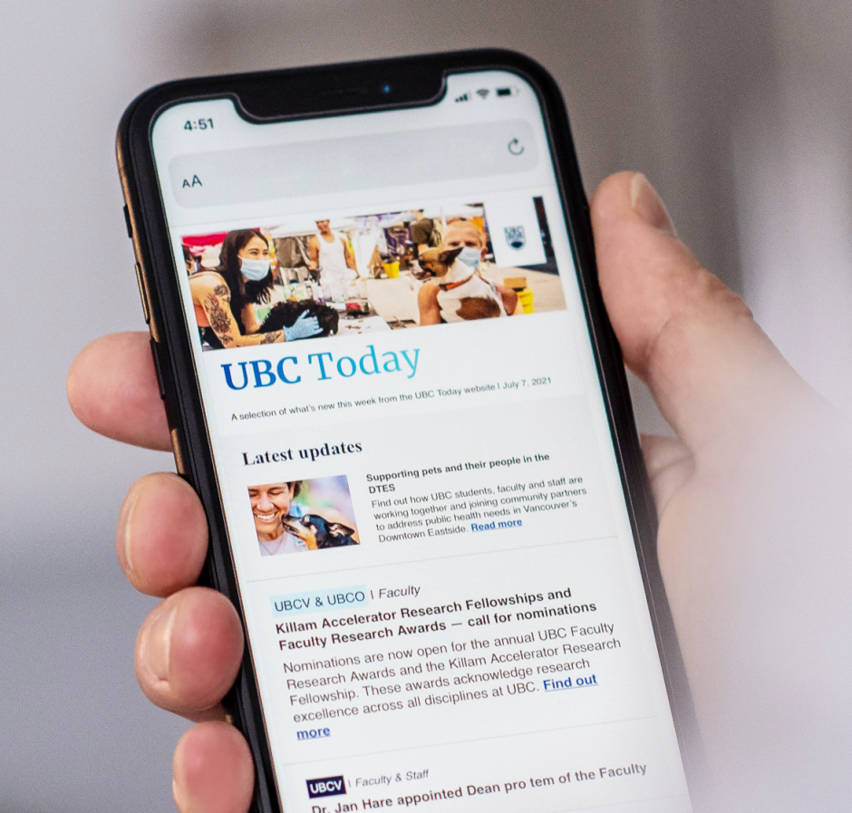 A hand holding a mobile device with the UBC Today website displayed on the screen